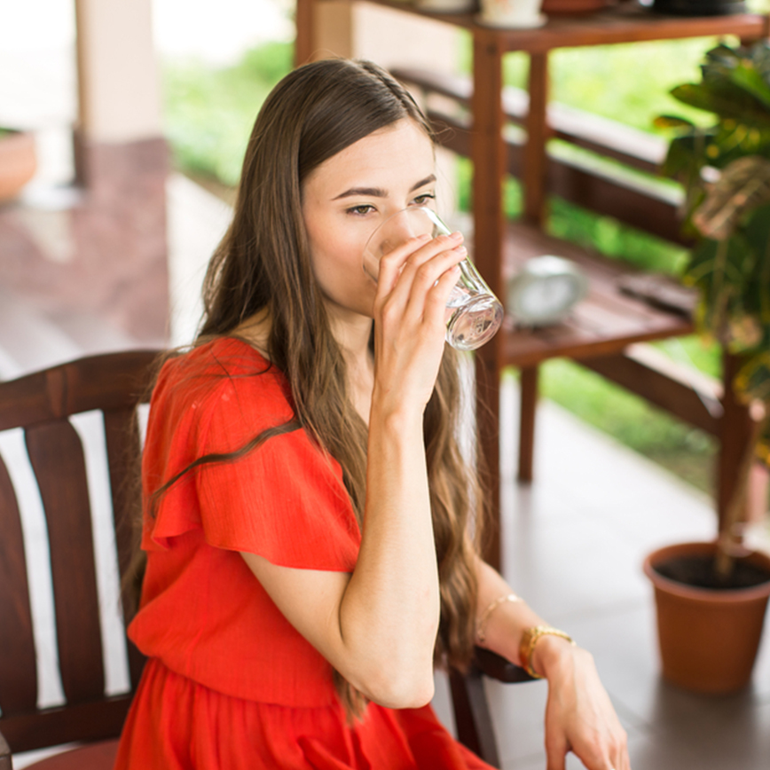Υποστηρίζει την υγεία του ουροποιητικού - Νεαρή γυναίκα κάθεται σε μια υπαίθρια αυλή και πίνει ένα ποτήρι νερό