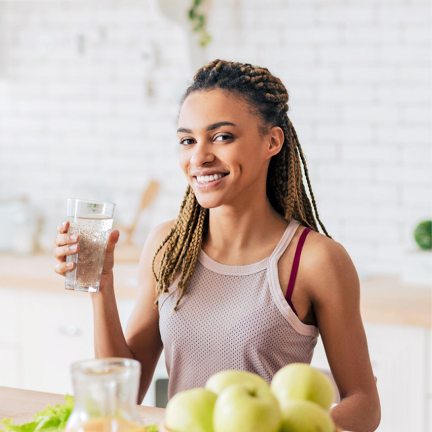Feel Light & Healthy – Νεαρή γυναίκα πίνει ένα ποτήρι νερό σε μια λευκή κουζίνα
